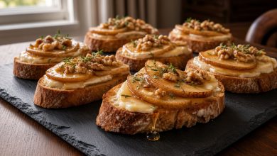 Brie and caramelized pear crostini on a slate board with honey drizzle, walnuts, and fresh thyme