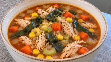 A stoneware bowl of chicken poblano soup with shredded chicken, dark roasted poblano strips, yellow corn, diced carrot and celery in a reddish-brown broth