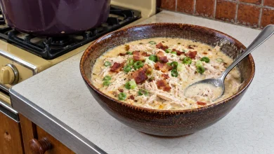 A bowl of creamy crack chicken soup with plenty of shredded chicken, crisp bacon pieces and sliced green onions, a spoon resting in the bowl