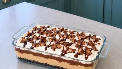 No-bake peanut butter lasagna in a 9x13 glass dish topped with whipped topping, chopped peanut butter cups and chocolate syrup