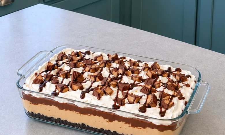 No-bake peanut butter lasagna in a 9x13 glass dish topped with whipped topping, chopped peanut butter cups and chocolate syrup